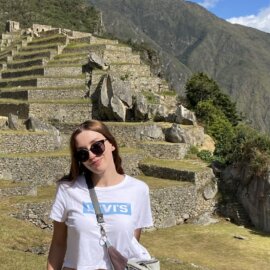 Katarzyna Wągrodzka stands in front of the ancient Incan ruins of Machu Picchu in Peru, wearing sunglasses and a white Levi’s t-shirt.