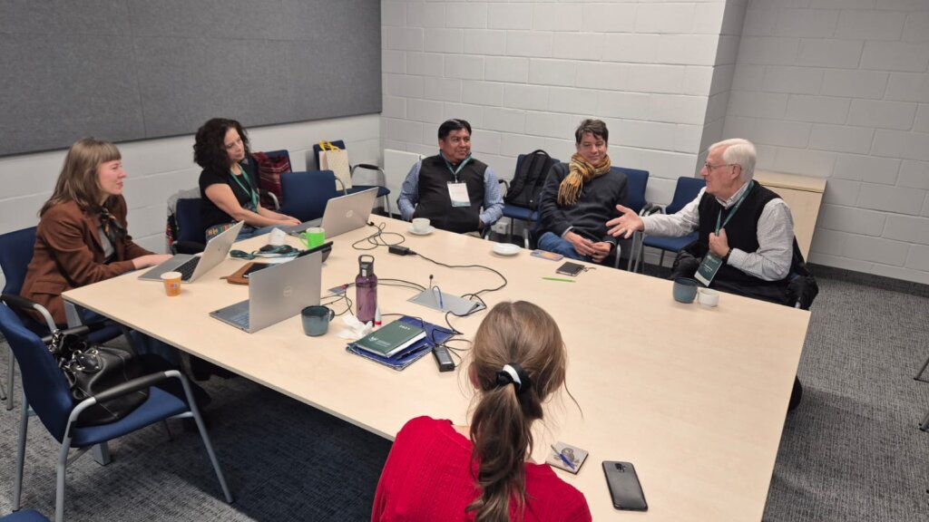 Participants of the workshop with Prof. John “Fritz” Schwaller and Eduardo de la Cruz Cruz — including Gabriela Piszczatowska, Agnieszka Brylak, Julia Madajczak, and Katarzyna Mikulska — sit around a conference table, engaged in discussion in a meeting room.