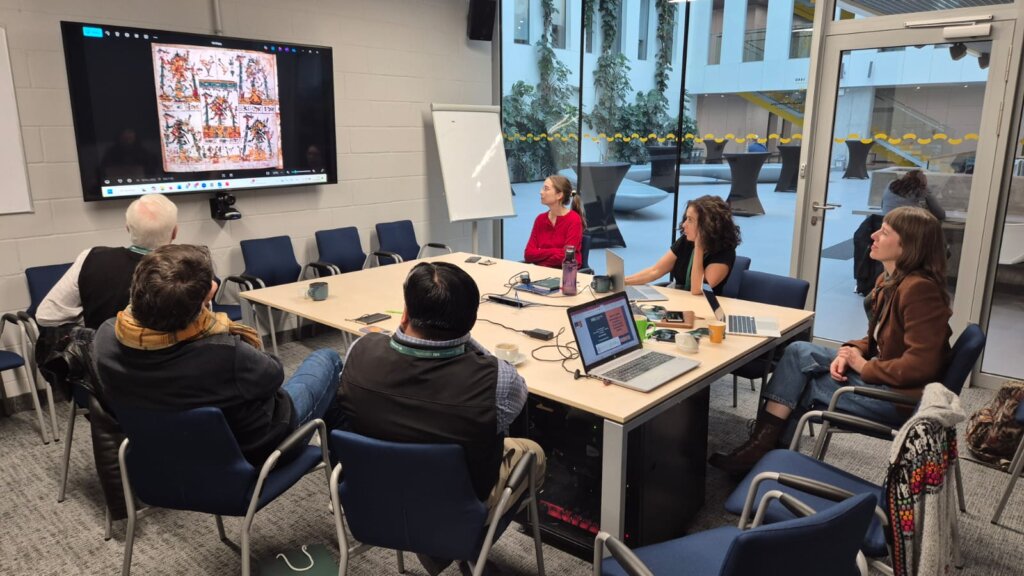 Participants of the workshop with Prof. John “Fritz” Schwaller and Eduardo de la Cruz Cruz — including Gabriela Piszczatowska, Agnieszka Brylak, Julia Madajczak, and Katarzyna Mikulska — sit around a conference table, analyzing a codex illustration shown on the screen.