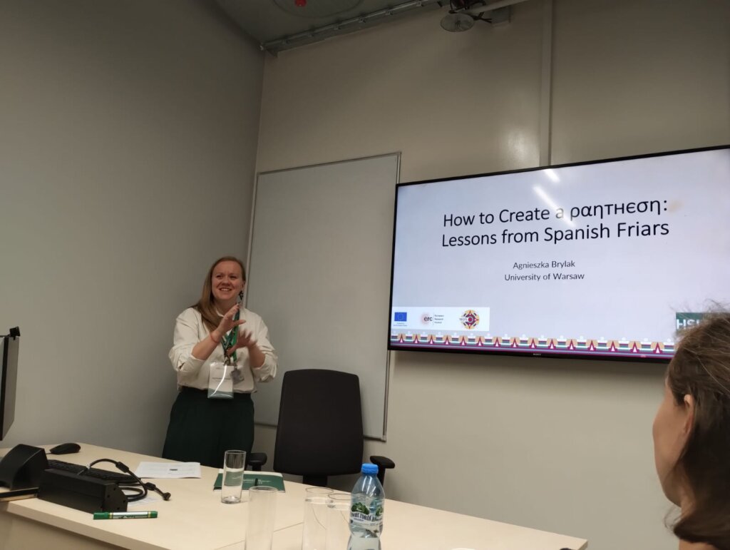 Agnieszka Brylak prezentuje temat „How to Create a ραητηση” w sali konferencyjnej, stojąc przed ekranem z wyświetlonym slajdem i uśmiechając się do publiczności.