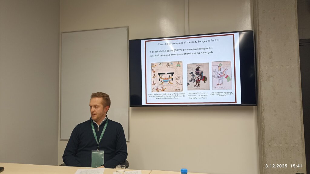 Matthijs Jonker siedzi przy biurku w sali konferencyjnej, a na ekranie wyświetla się slajd zatytułowany „Recent interpretations of the deity images in the FC”, dotyczący europeizacji ikonografii i antropomorfizacji bogów Azteków.