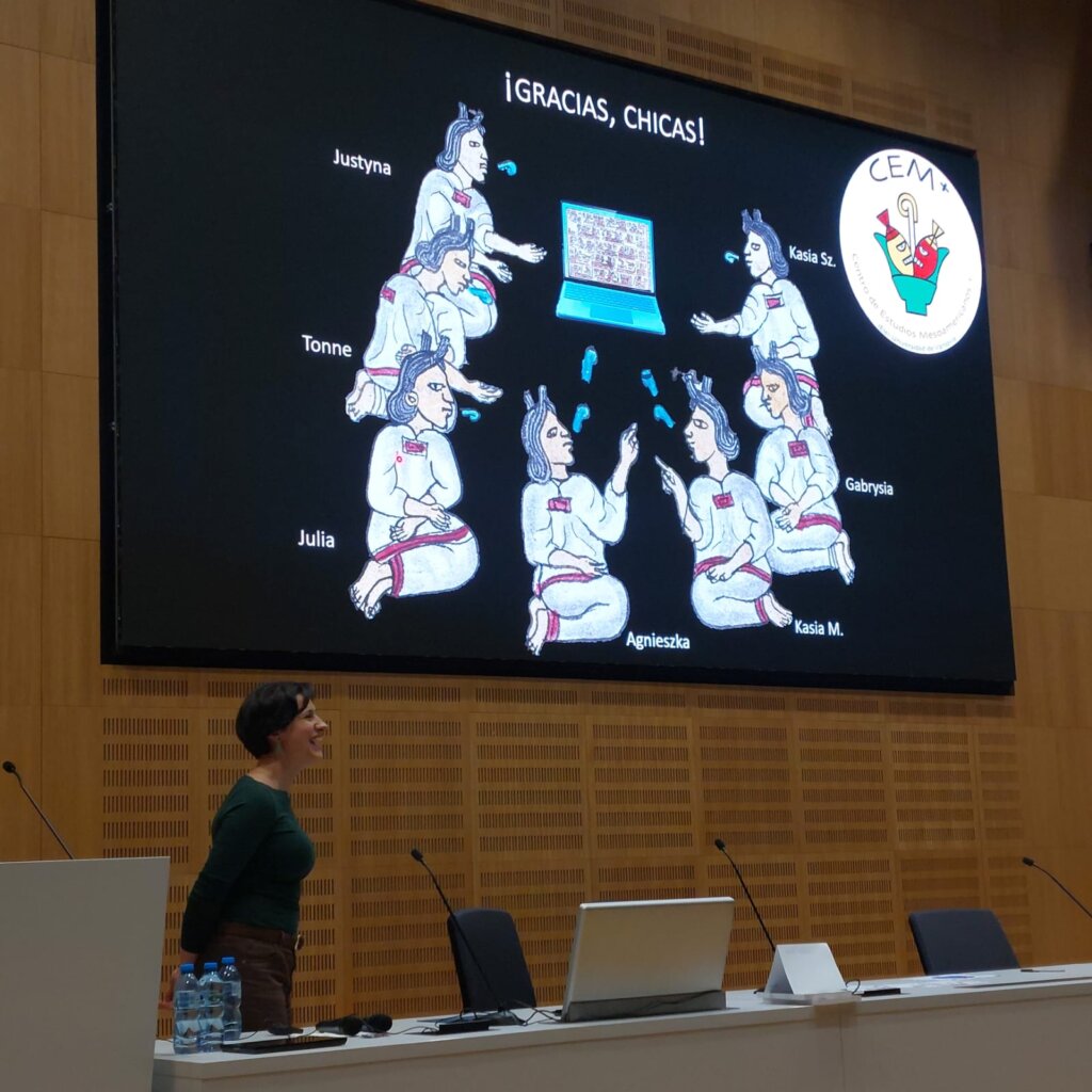 Justyna Kowalczyk-Kądziela stoi uśmiechnięta przed ekranem w sali konferencyjnej, na którym wyświetla się slajd z ilustracją ośmiu kobiet z podpisem „¡GRACIAS, CHICAS!” i logotypem Círculo de Estudios Mesoamericanos.