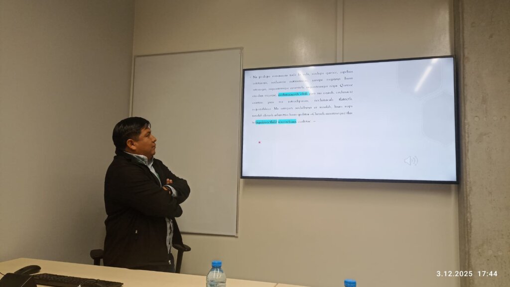 Eduardo de la Cruz stoi przy biurku w sali konferencyjnej i patrzy na ekran, na którym wyświetla się slajd z tekstem w języku nahuatl.