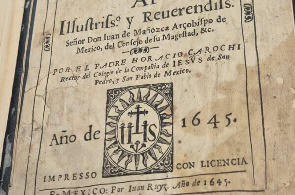 La página de título del libro impreso en 1645 Arte de la lengua mexicana, con una hoja envejecida y un emblema IHS.